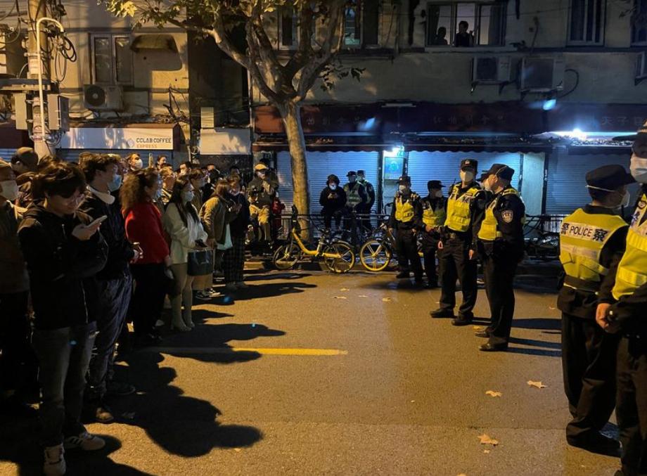 Un groupe de personnes se tient devant une file de policiers lors d'une manifestation contre les contrôles du COVID-19