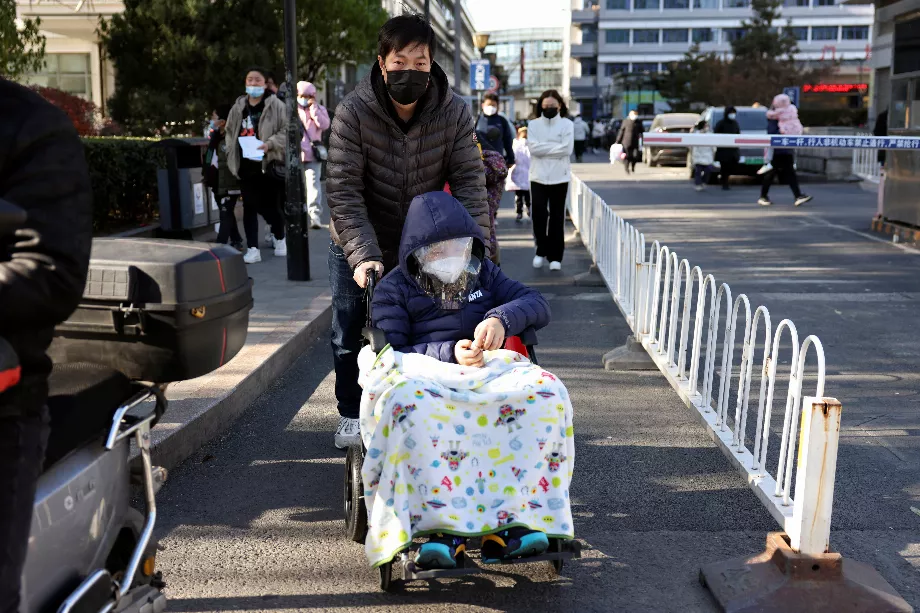 Un homme pousse un enfant recouvert d'une couverture dans un fauteuil roulant devant un hôpital pour enfants à Pékin, en Chine, le 24 novembre 2023 (REUTERS/Florence Lo)